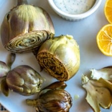 A white plate with artichokes on it and a white dish with flavored mayonnaise and a lemon cut in half on the plate.