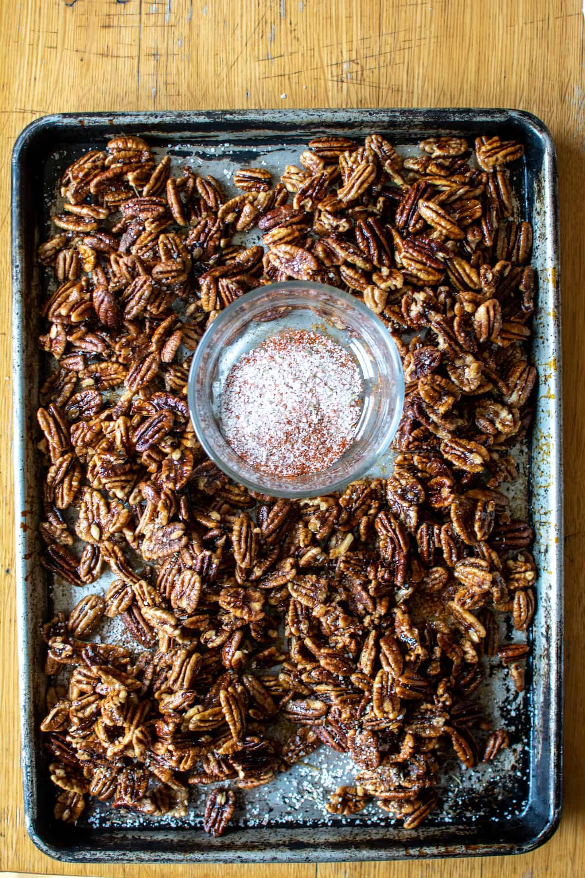 A metal baking sheet with candied pecans on them and a bowl of cayenne salt in the middle.