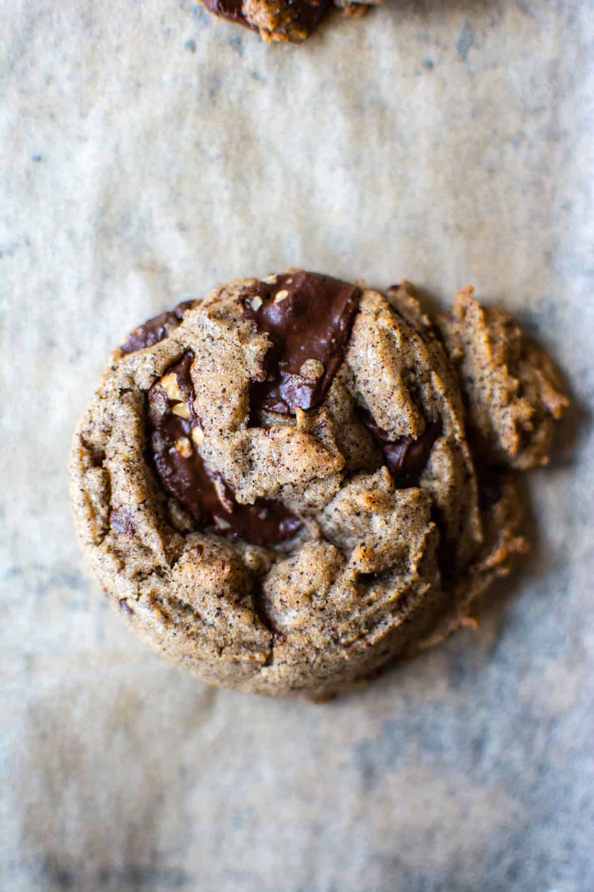 A coffee bean chocolate chip cookie sitting on a parchment lined baking sheet.