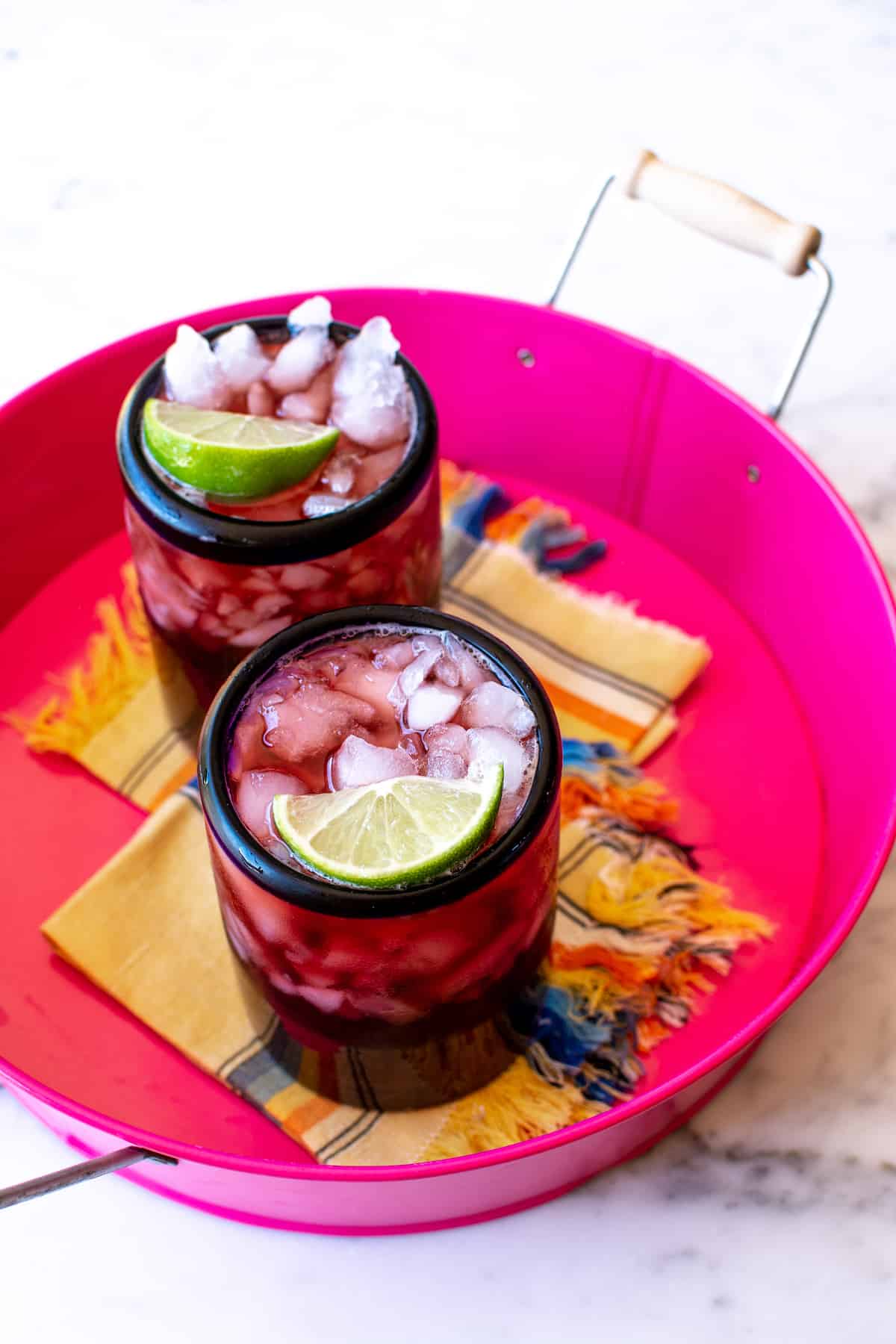 Two glasses of Agua de Jamaica in a pink tray with two yellow napkins on the bottom.