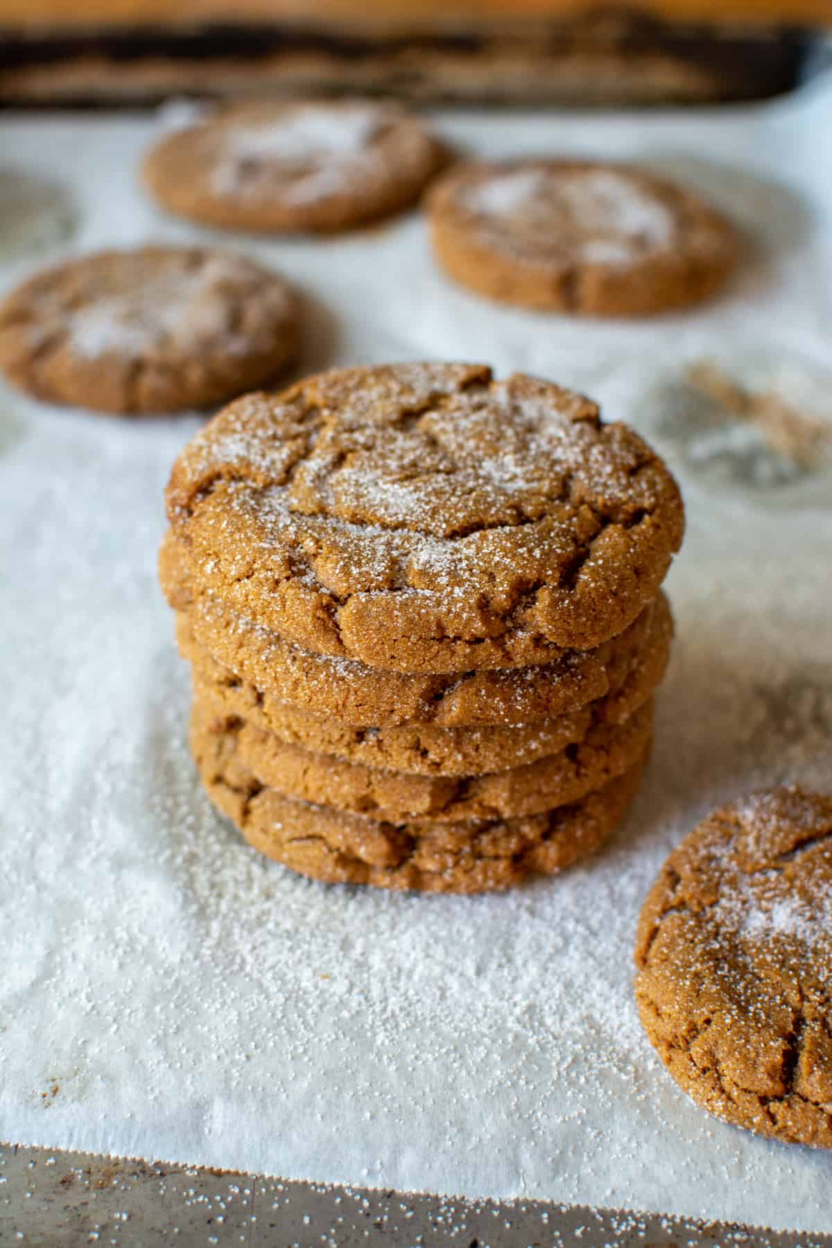A tall stack of molasses cookies sitting on a parchment-lined baking sheet.