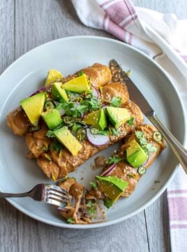 A plate of enchiladas with avocado on top