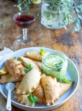 A plate of beef empanadas next to a glass of wine