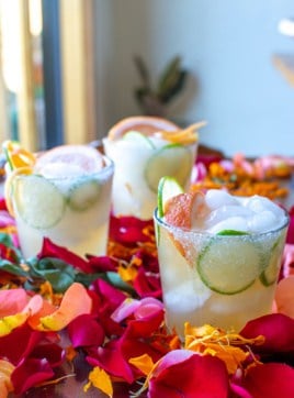 three margaritas sitting on a table with flower petals.