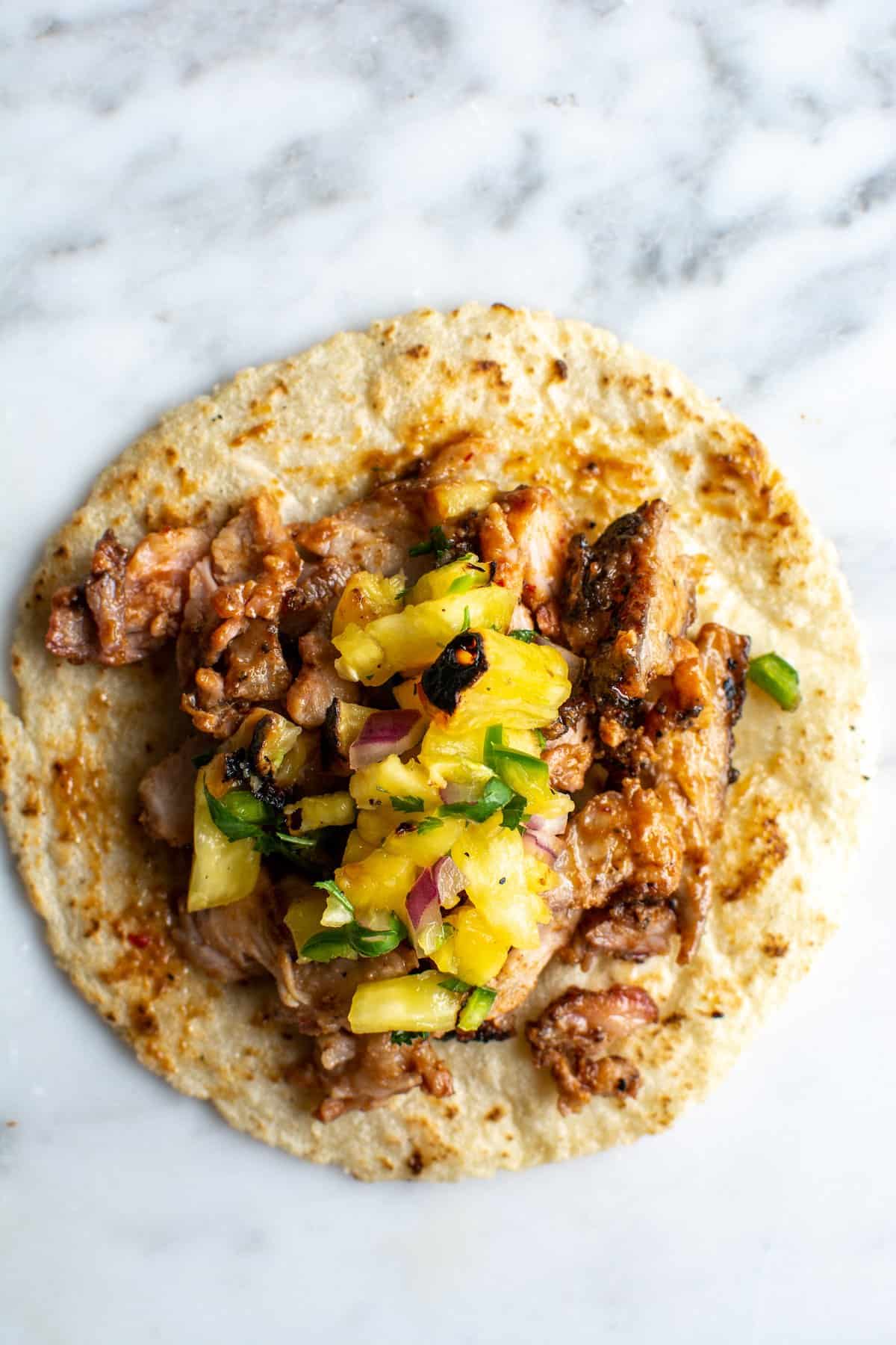 One taco al pastor topped with grilled pineapple salsa sitting on a marble table.