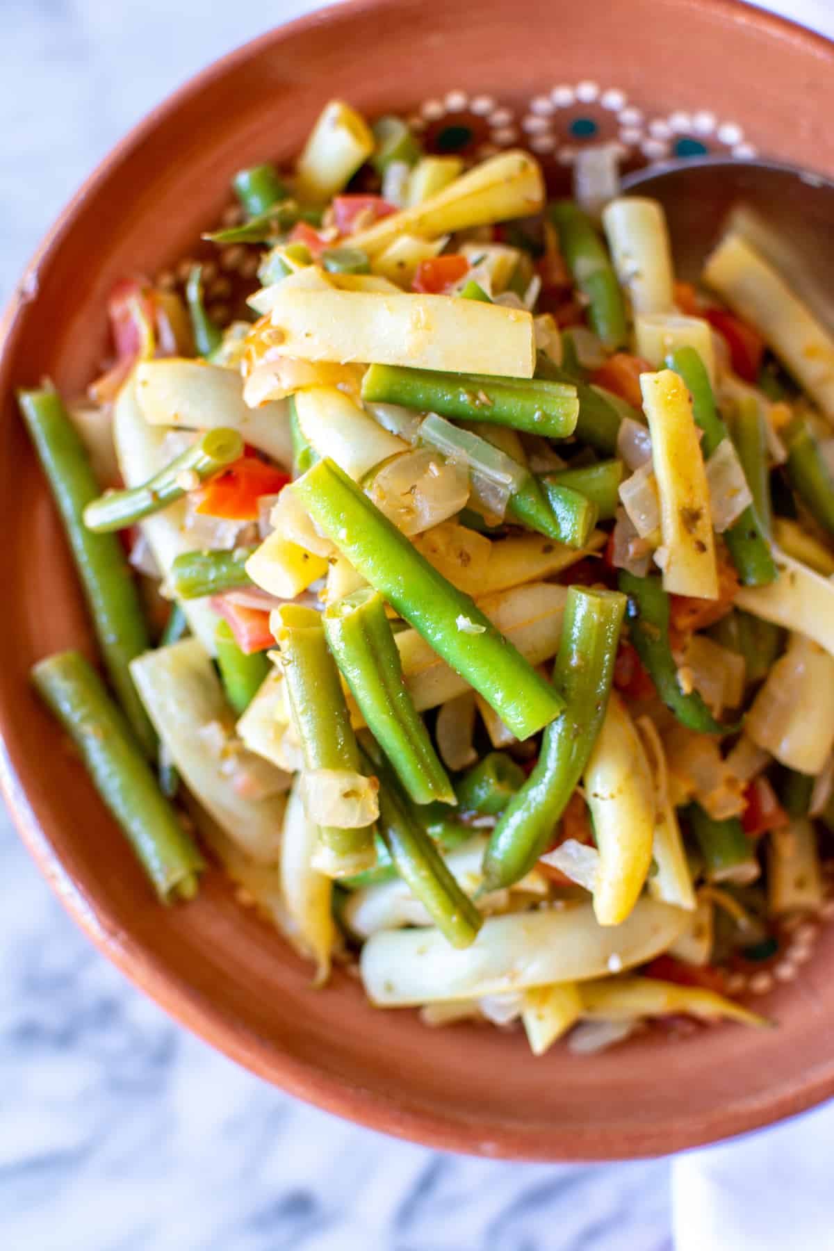 A terracotta bowl filled with green beans and yellow wax beans sautéed with tomatoes and onions.