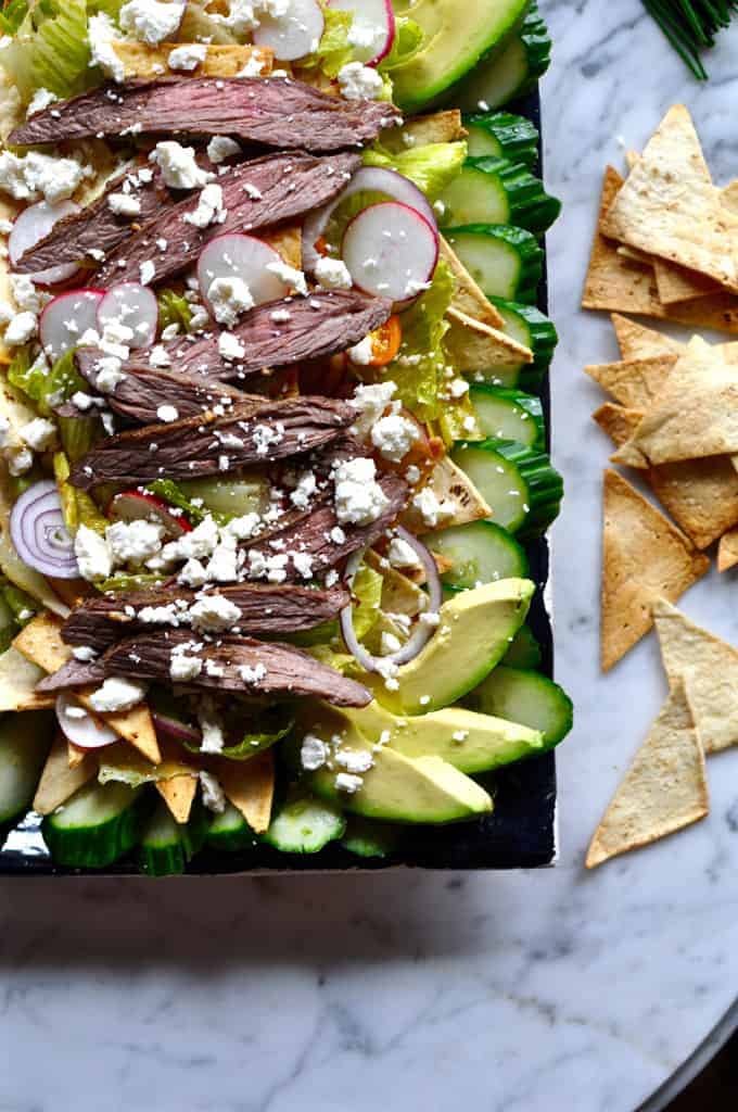 This recipe combines Salpicon salad and Fattoush salad with seasoned steak, oven-baked flatbread crisps, avocado, feta cheese, and spicy chipotle dressing.