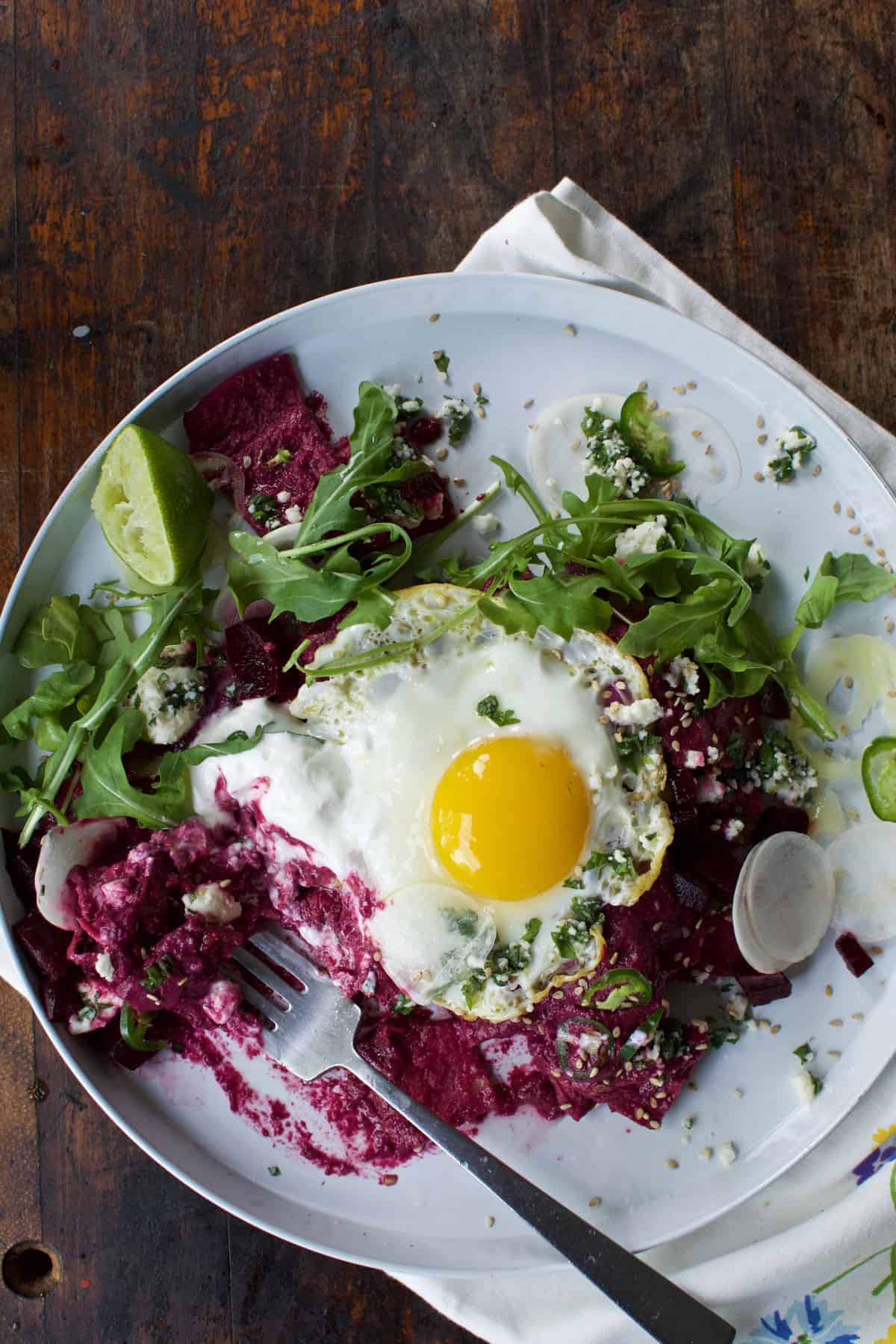 These beet chilaquiles with fried eggs are crisp tortillas covered in a spicy beet salsa then topped with a crumbly herb cheese, sour cream, and fried eggs.