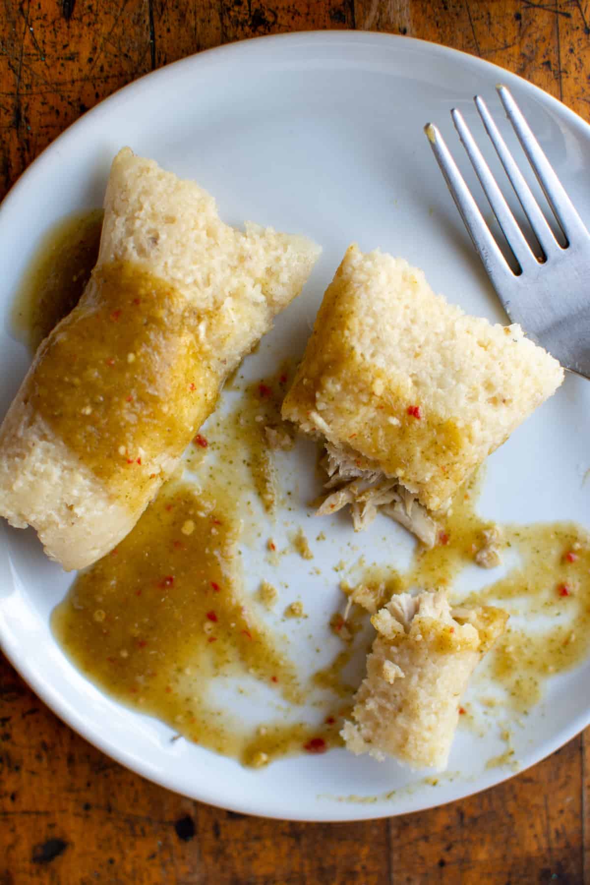 Two tamales on a white plate with salsa verde drizzled on top and a fork on the side of the plate.