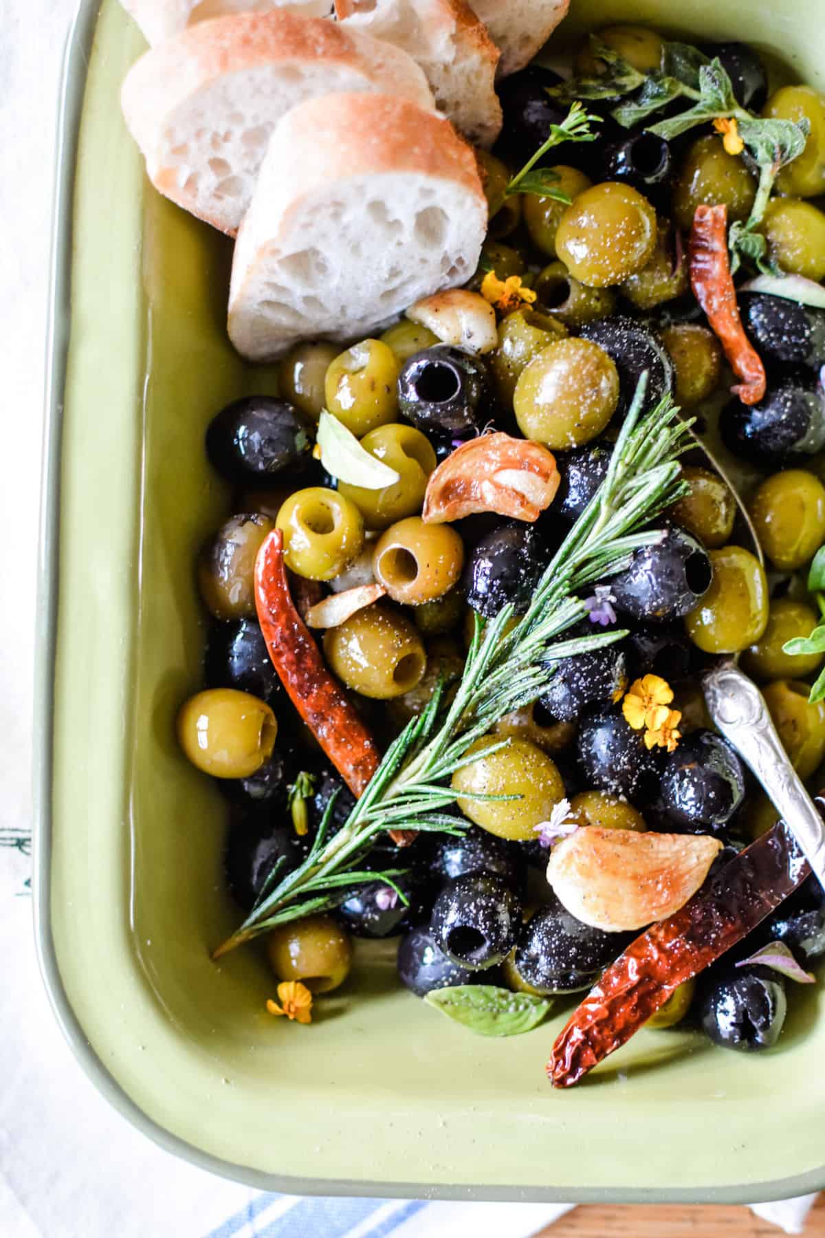 Olive Lovers Unite! You've got to try these Spicy Marinated Olives with fiery dried arbol chiles, pan-roasted cloves of garlic and loads of fresh herbs like rosemary and oregano. Fix this when you need a quick, easy & comforting appetizer to share with friends that will disappear in minutes. Serve warm or make ahead and serve room temperature with slices of crusty baguette for scooping. {gluten-free, grain-free, and vegan} #olives #marinatedolives #spicy #appetizer #roastedgarlic #easyappetizer