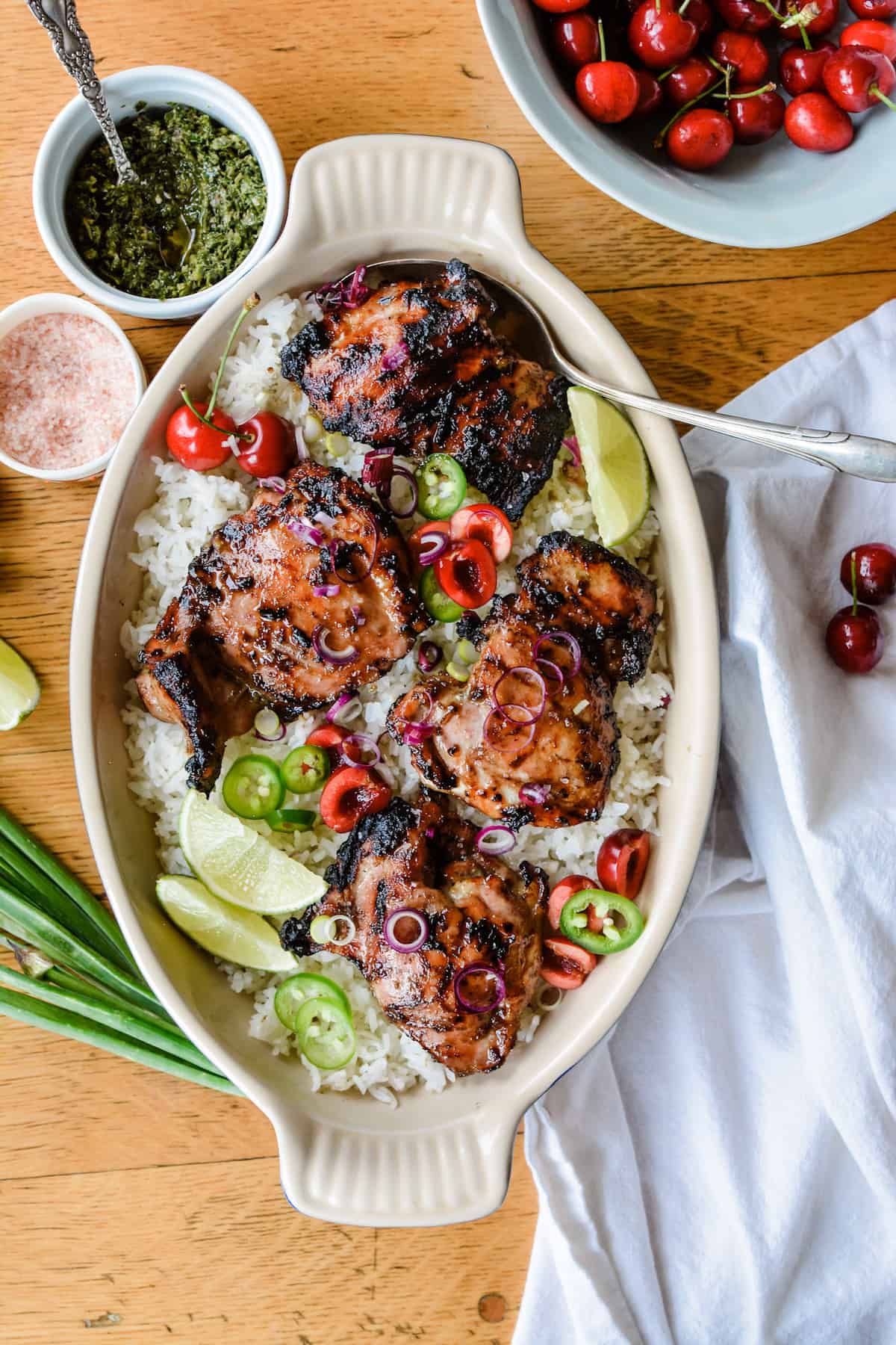 A dish of chicken and rice sitting on a wooden table with cherries.