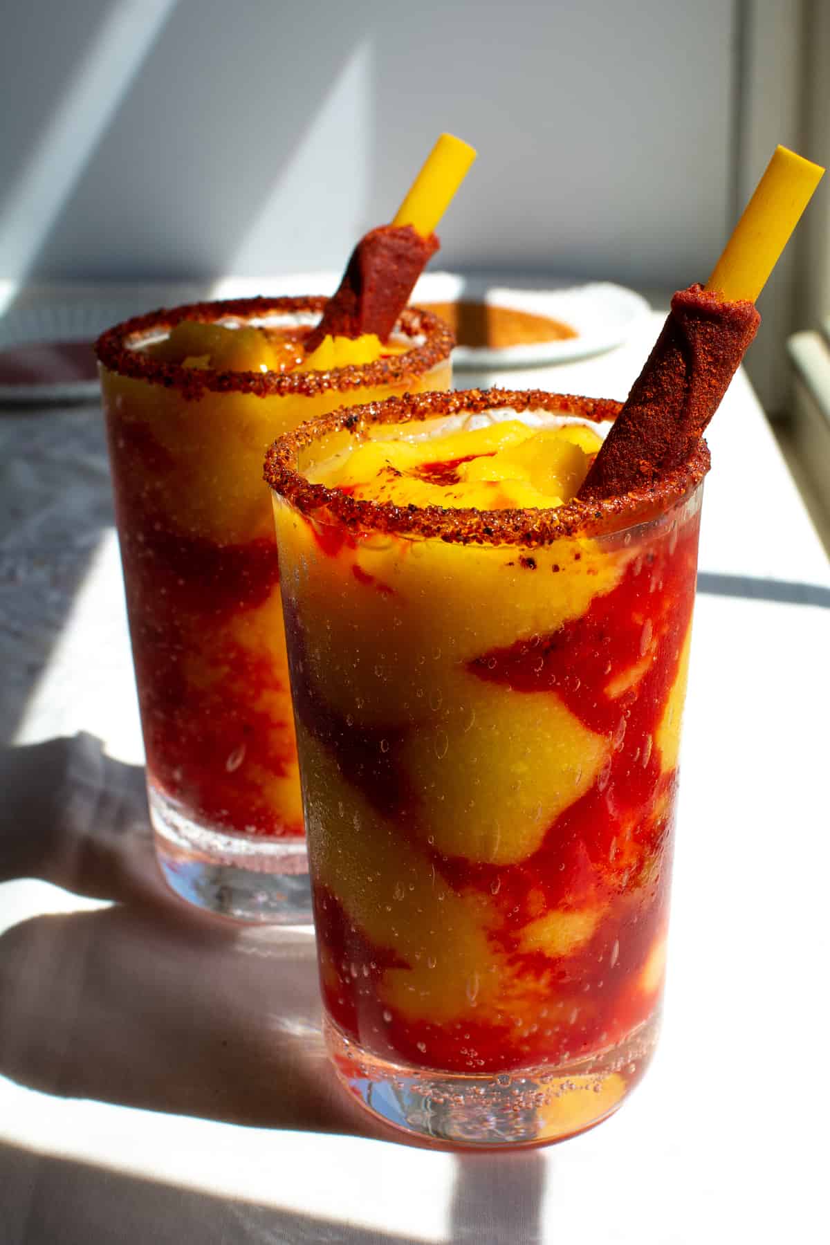 How to make a Mangonada! If you've ever had this sweet, sour, salty mango slushy than you know how perfect it is on a hot day. Layers of frozen mango smoothie, Chamoy sauce and Tajin. So easy and so satisfying, bring it on summer! #mangonada #mangosmoothie #mexicancuisine #mangoslushy