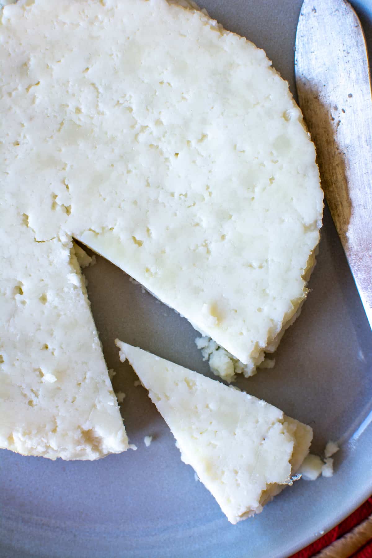 A wheel of Panela cheese with a wedge cut out sitting on a white plate with a knife on the side.