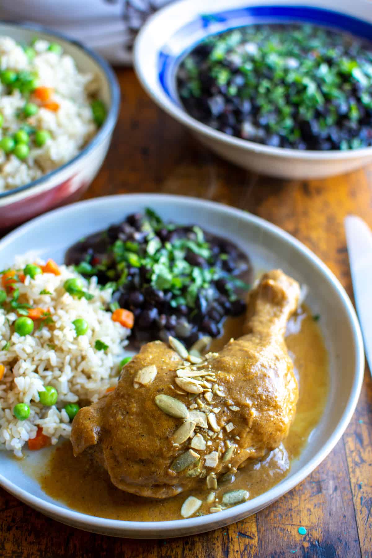 A plate of chicken covered with pumpkin mole and a side of rice and black beans.