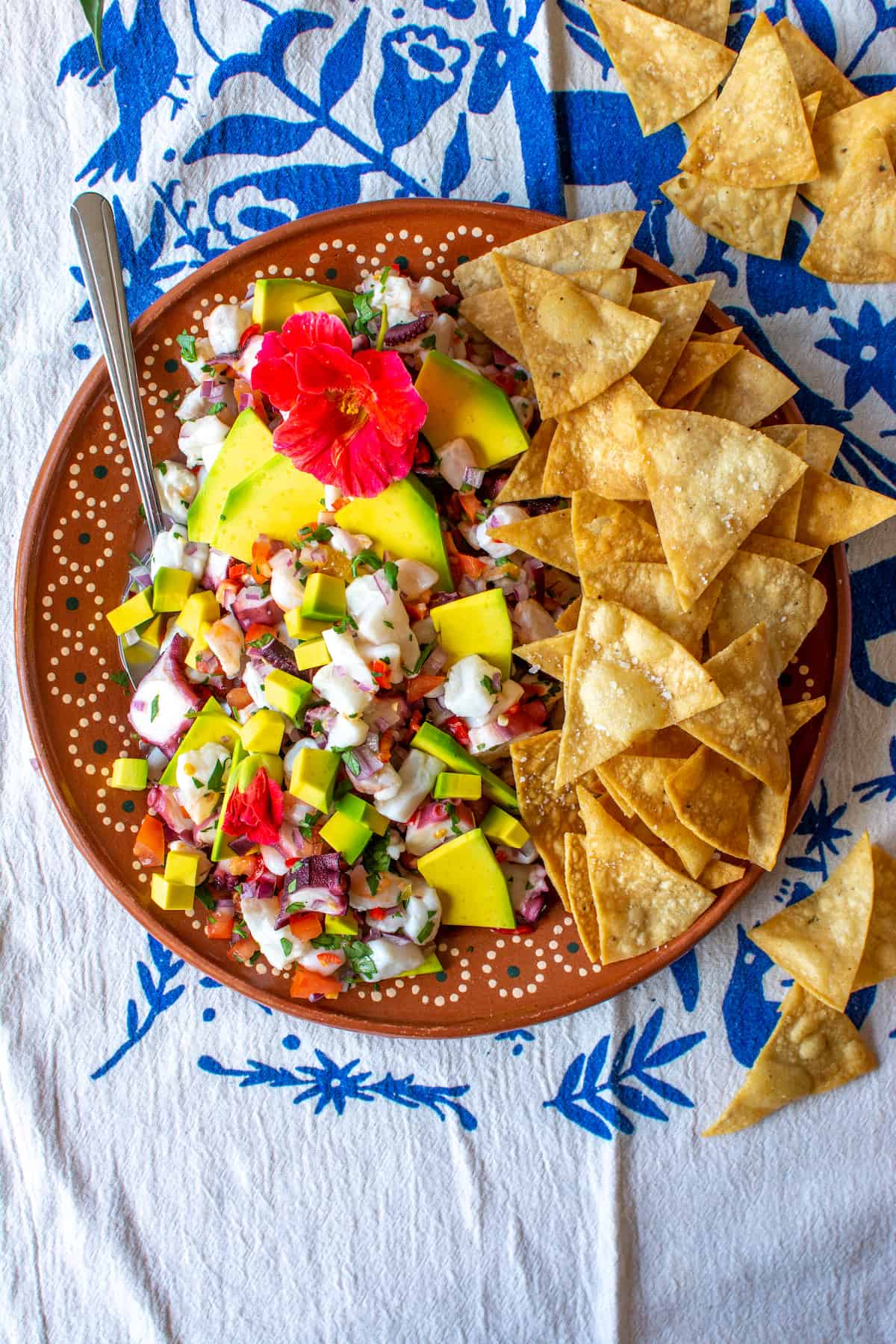 A terracotta plate filled with seafood ceviche and tortilla chips sitting on a blue and white tablecloth.