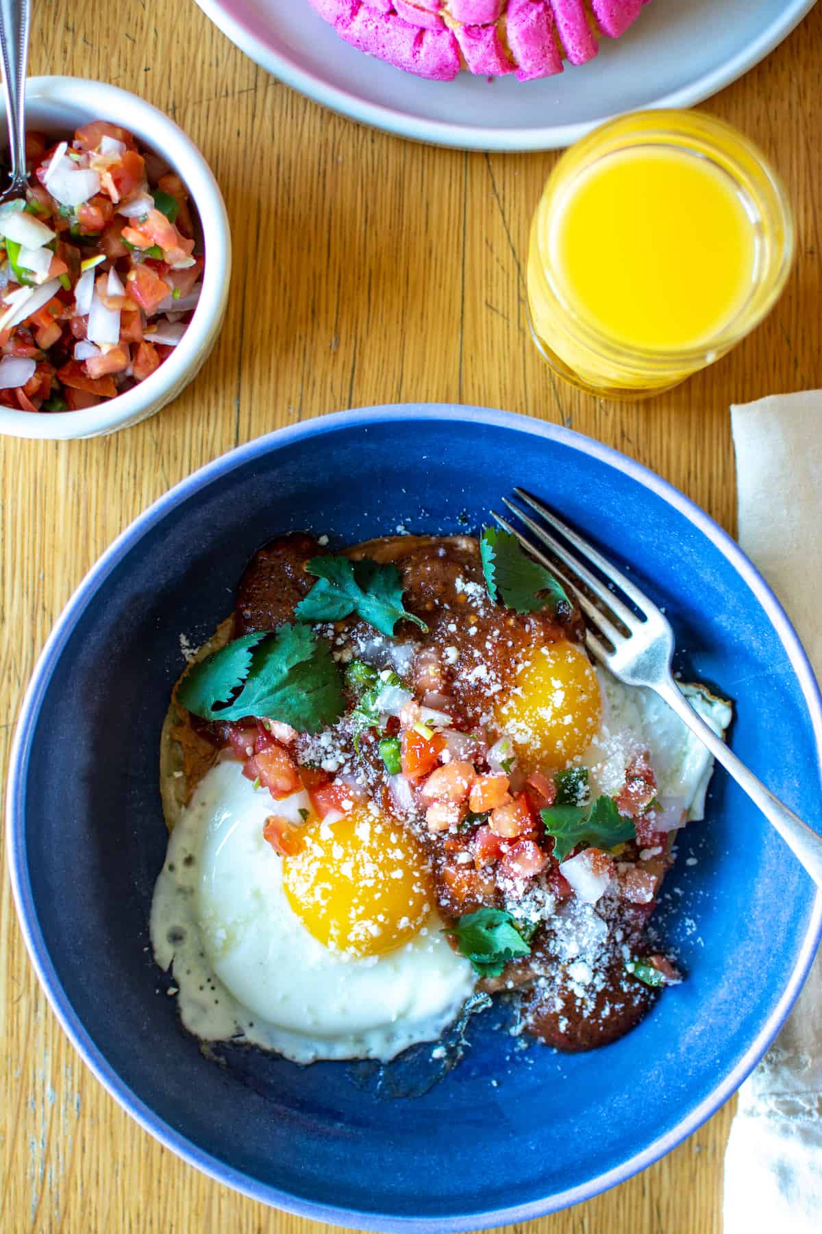 A blue plate of Huevos Rancheros on a kitchen table with orange juice.