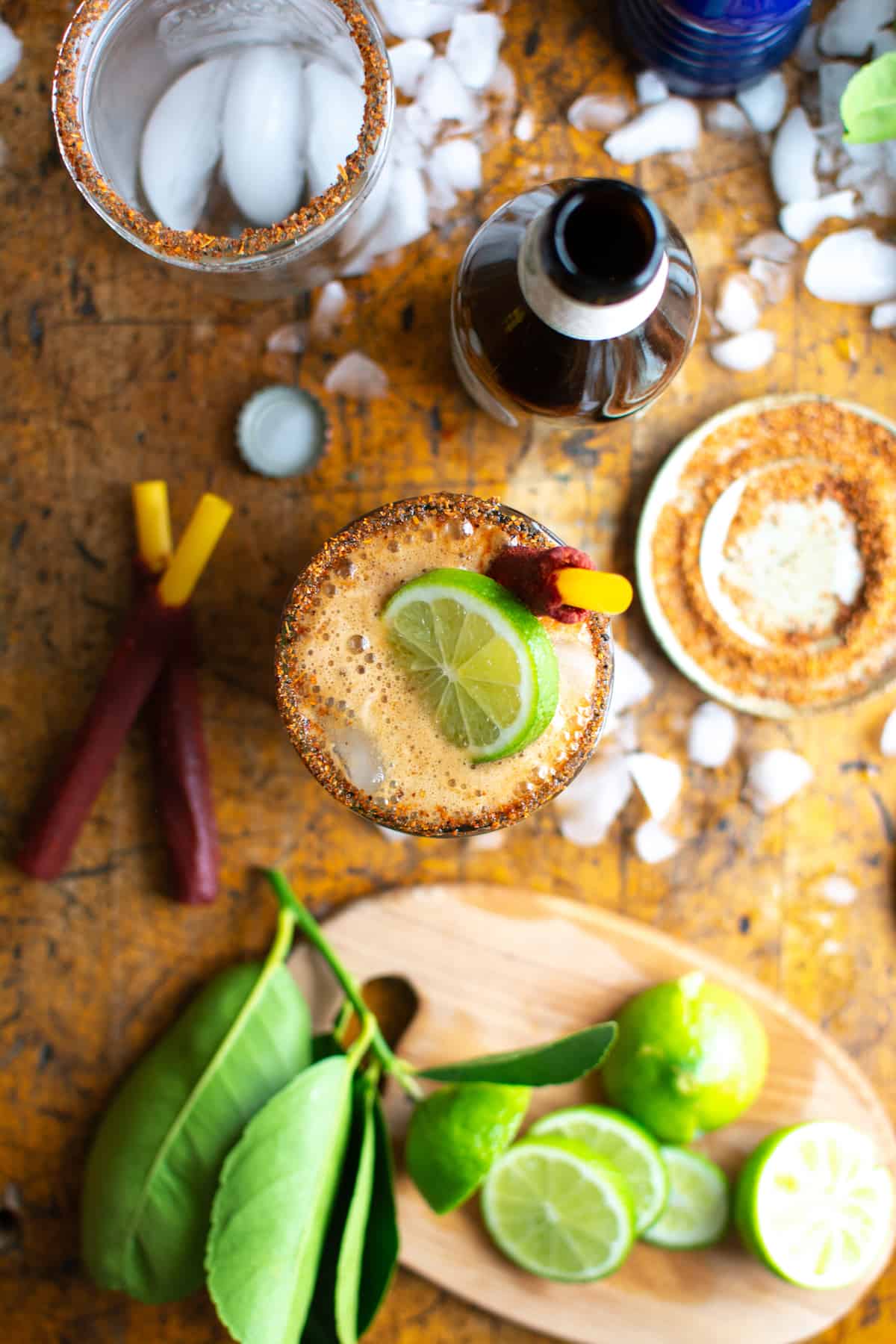 An overhead shot of a michelada with a tamarind straw and a lime slice in the glass on a wood table.