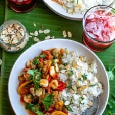 Two plates of Veracruz-style Hominy recipe with white rice on banana leaves with purple drinks next to the plates.