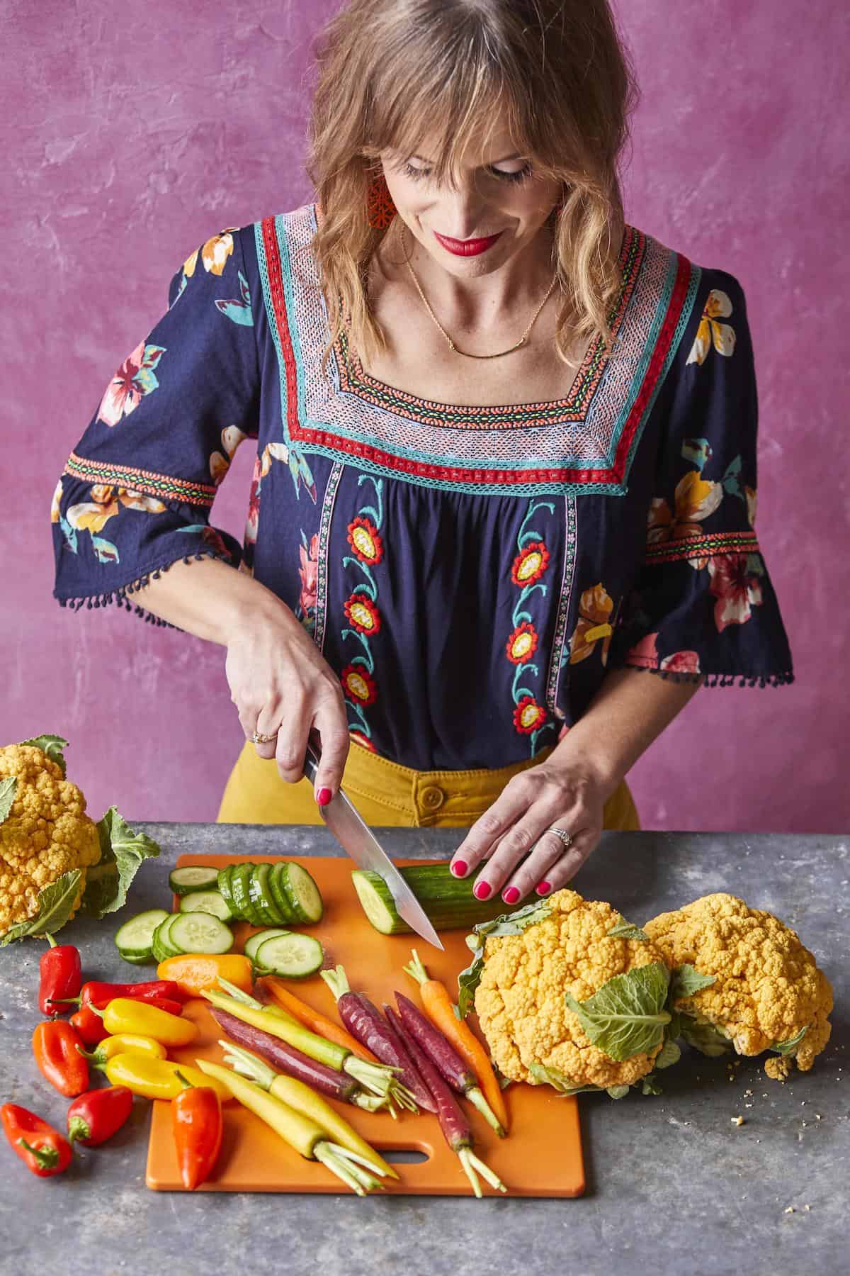 A woman chopping vegetables in a blue shirt with a pink background.