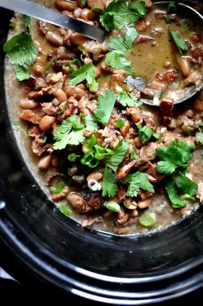 A black pot filled with frijoles borrachos topped with cilantro leaves.