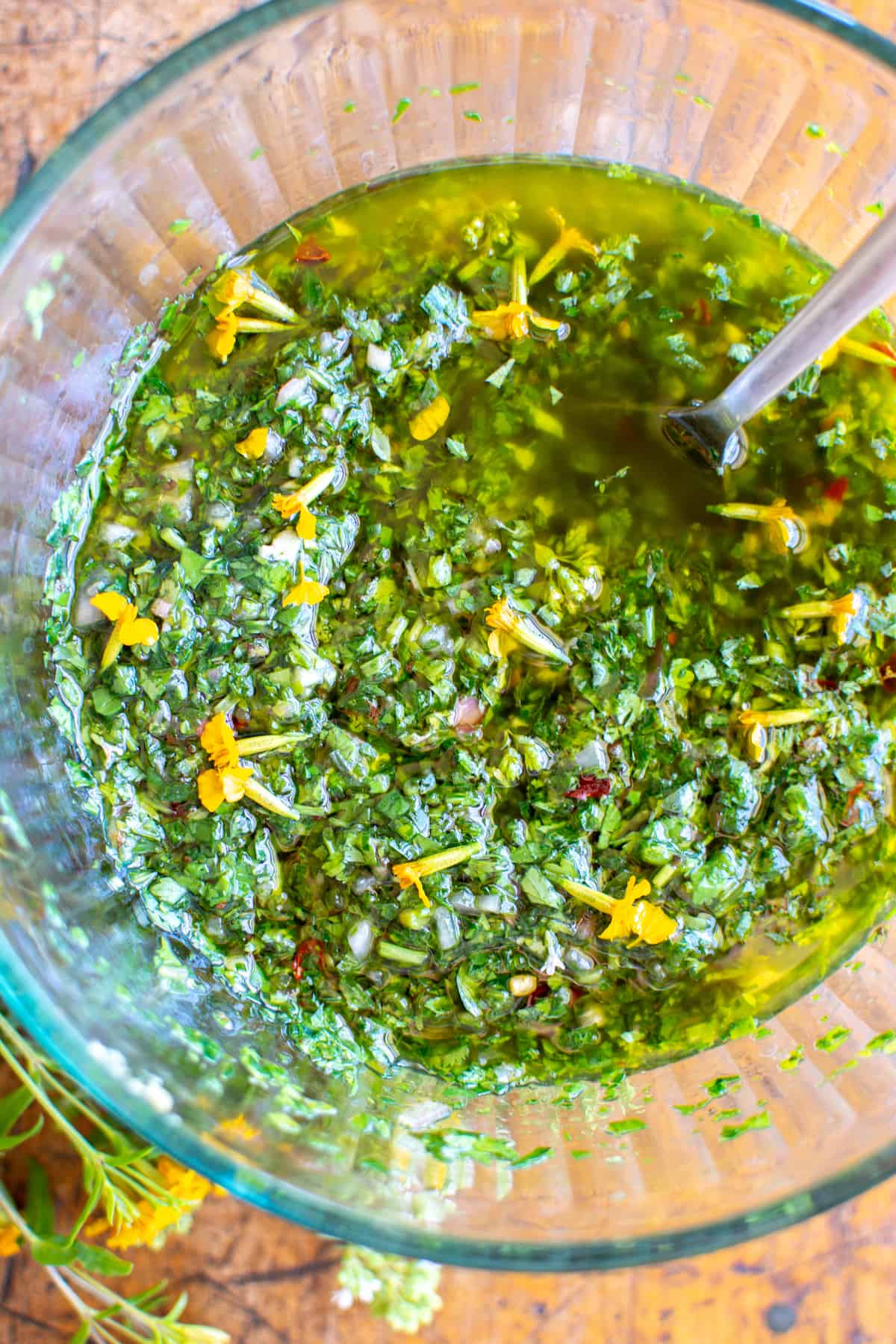 A glass bowl with chimichurri sauce in it with a spoon sticking out of one side of the bowl.