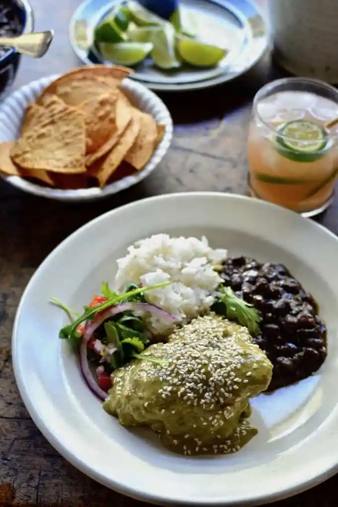 A white plate with chicken mole verde on it and a side of black beans.