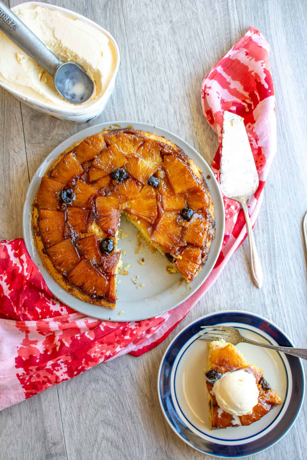 A pineapple upside down cake with a piece cut out and sitting on a plate next to it.