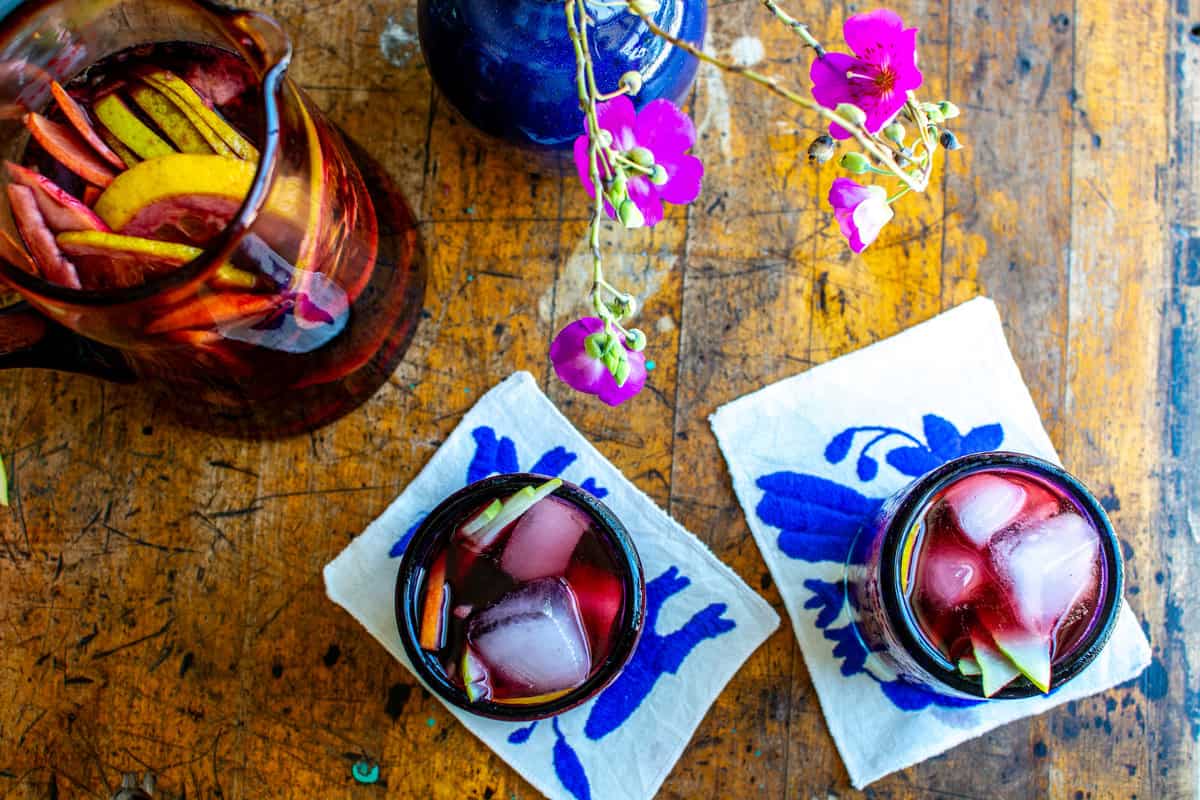 Two glasses of sangria on two blue Otomi cocktail napkins on a wood counter.