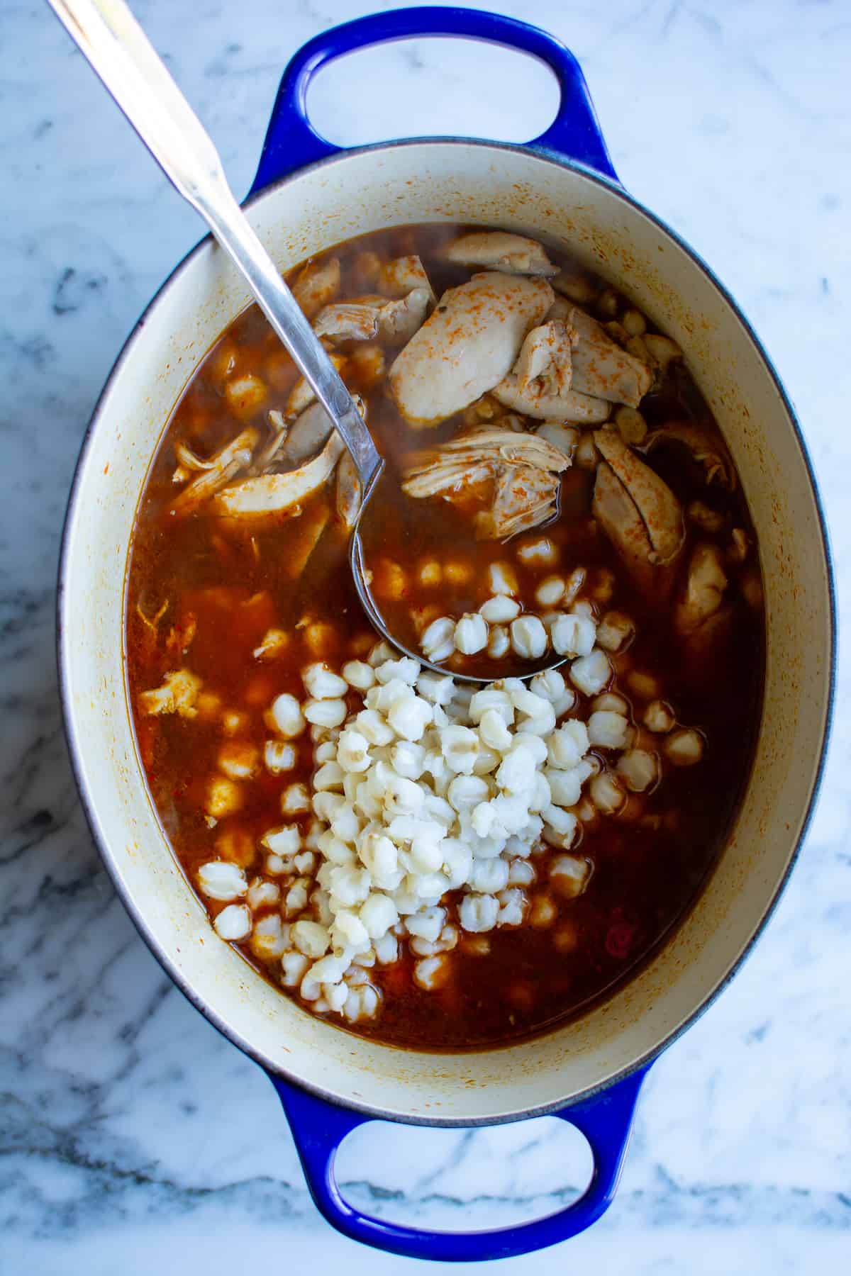 A pot of chicken pozole with a ladle in the pot.