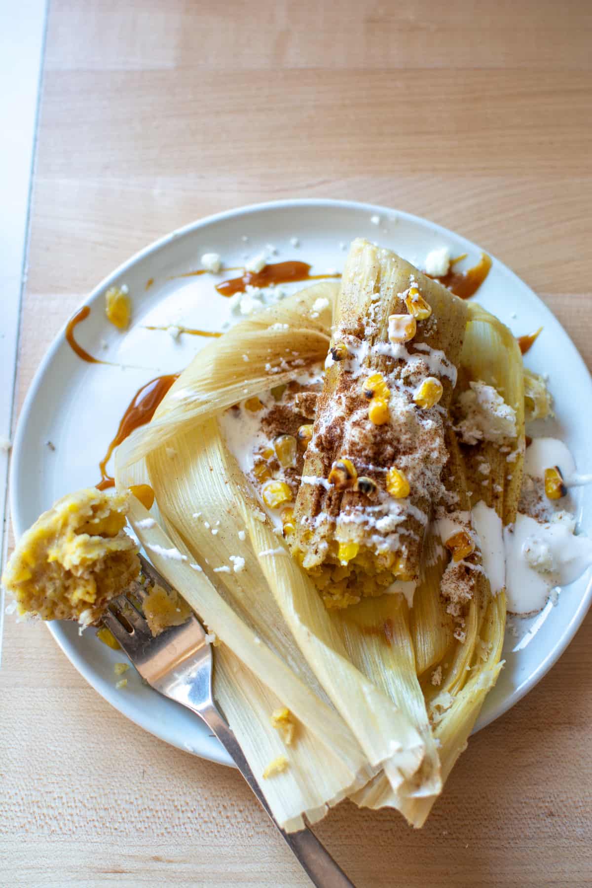 A corn tamal on a white plate topped with crema and cinnamon