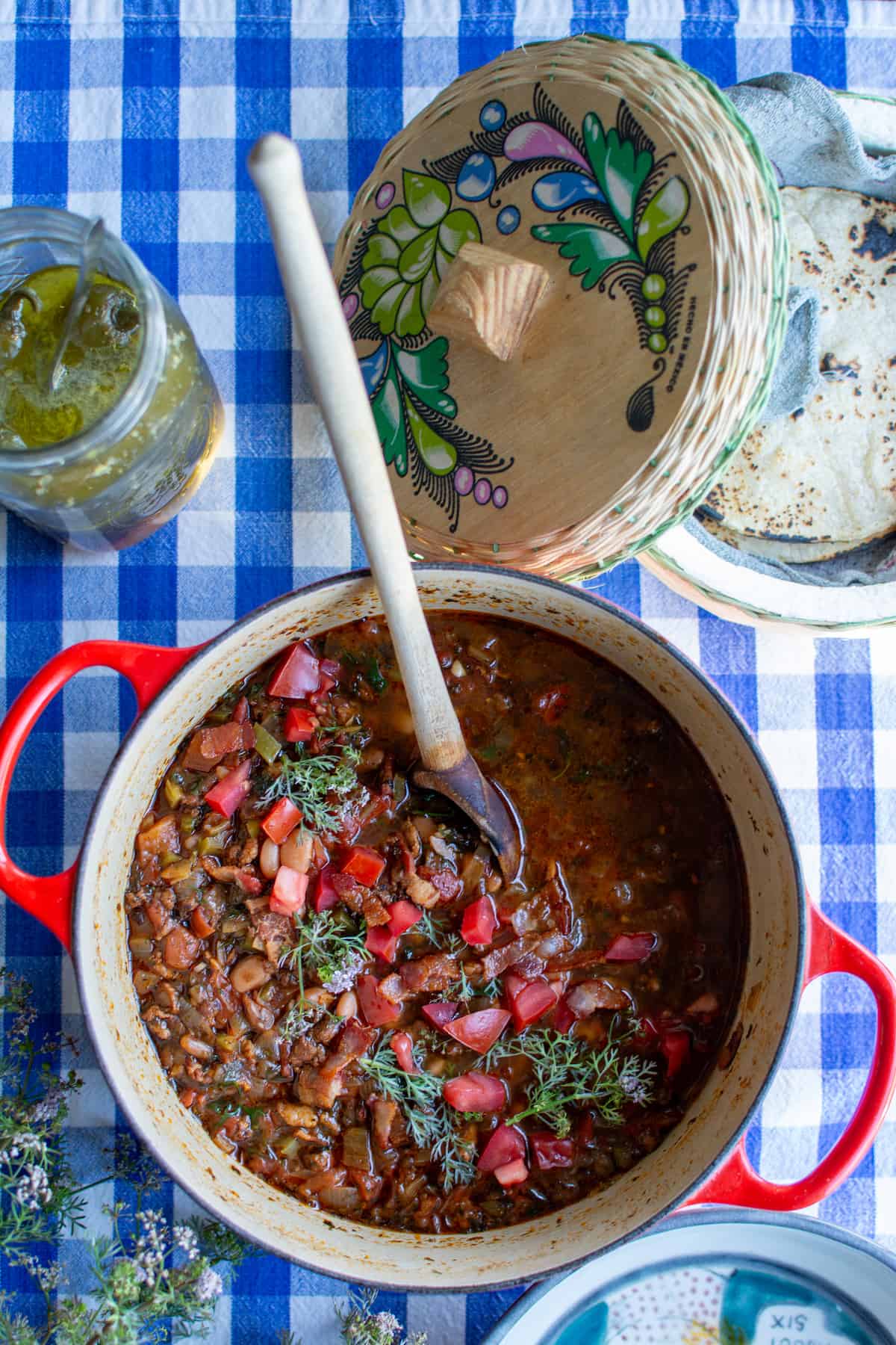 A pot of frijoles charros recipe on a blue and white checked tablecloth