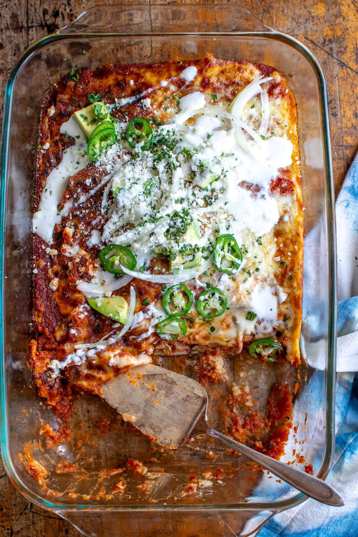 A pan of refried bean enchiladas with a piece missing.