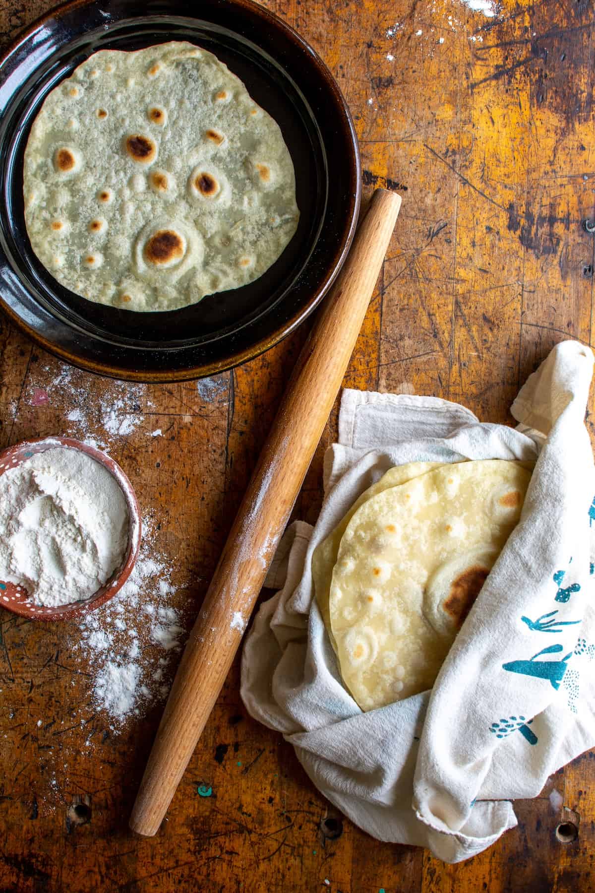 A stack of flour tortillas wrapped in a towel with a rolling pin next to it.