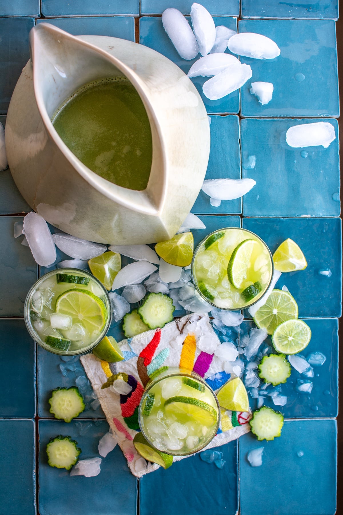 Three glasses of cucumber lime agua fresca on a blue tile table