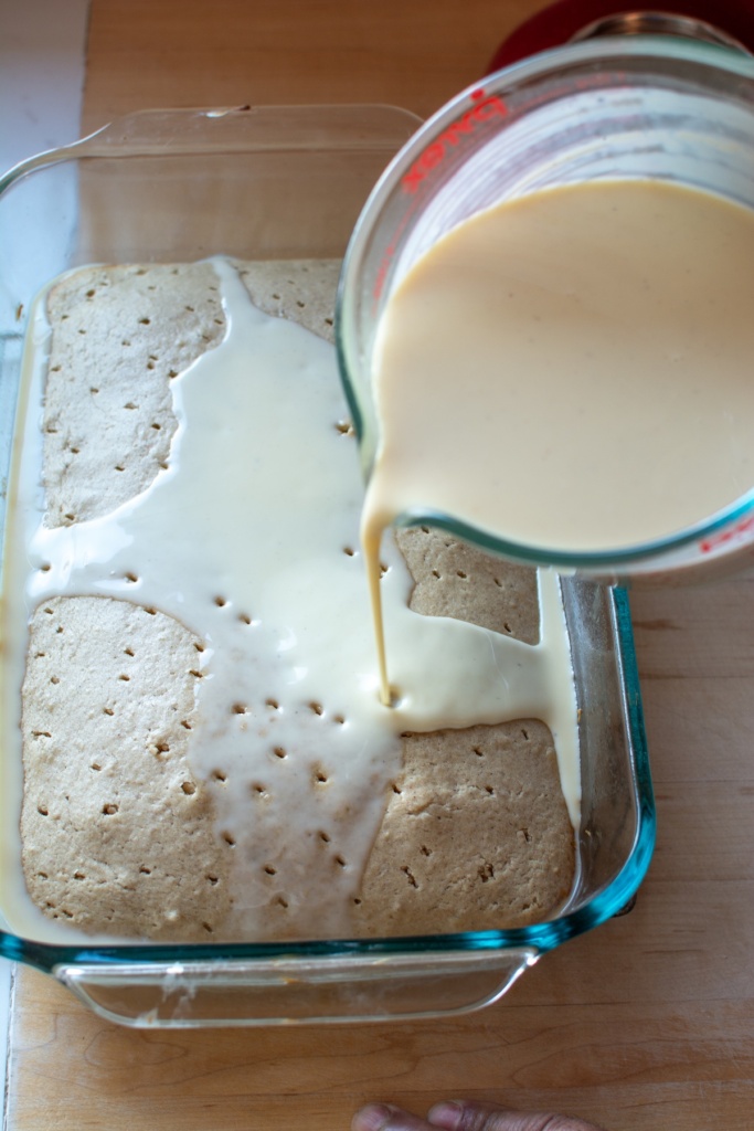Tres leches mixture being poured over the cake