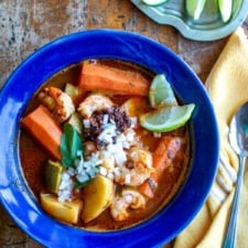 A bowl of Caldo de Camarón topped with fresh lime wedges