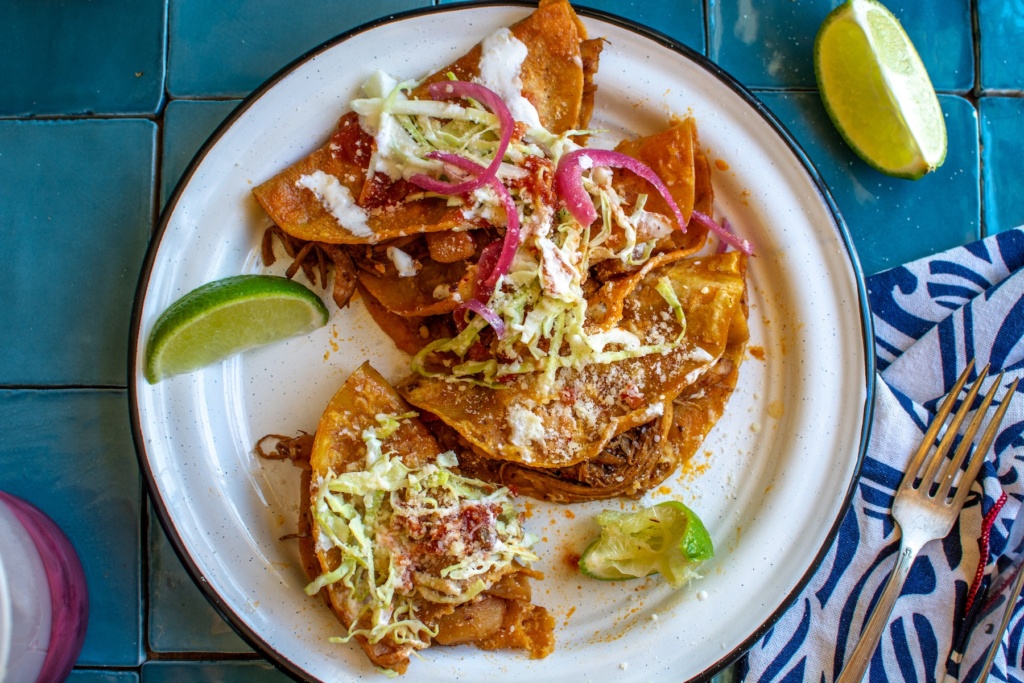 Tacos al vapor on a white plate with a bite taken out of it. 