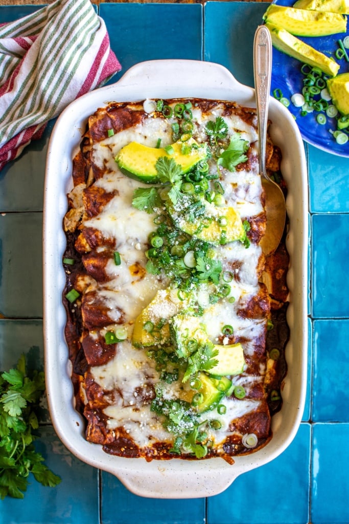 A baking dish of chicken enchiladas topped with avocado