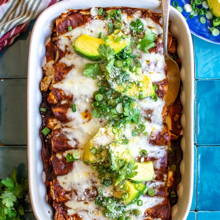 A baking dish of chicken enchiladas topped with avocado