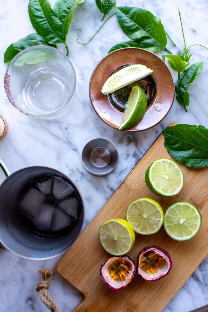 a cocktail shaker with limes and passion fruit next to it. 