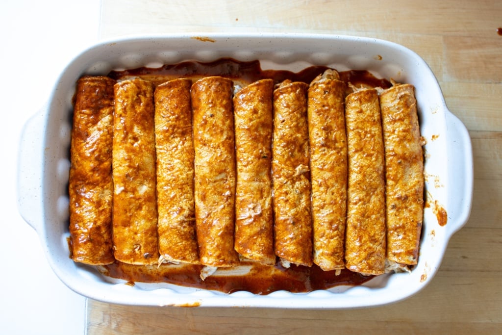 A baking dish with enchiladas lined up in it. 