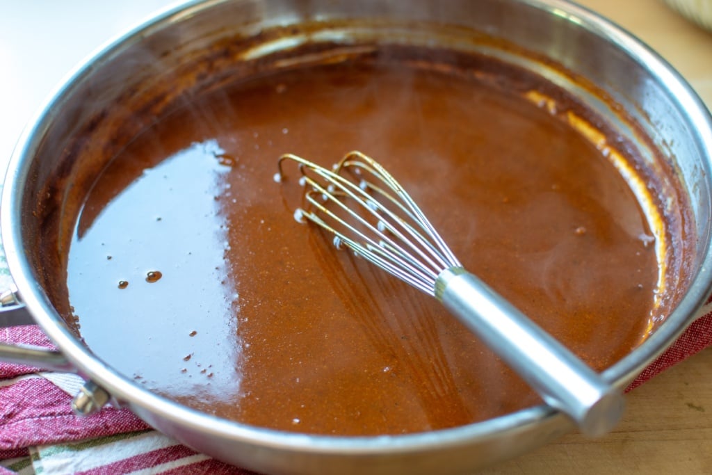 red enchilada sauce in a skillet with a whisk in it. 