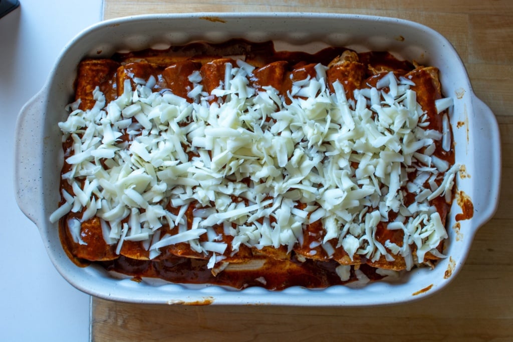 The enchiladas in a baking dish topped with shredded cheese. 