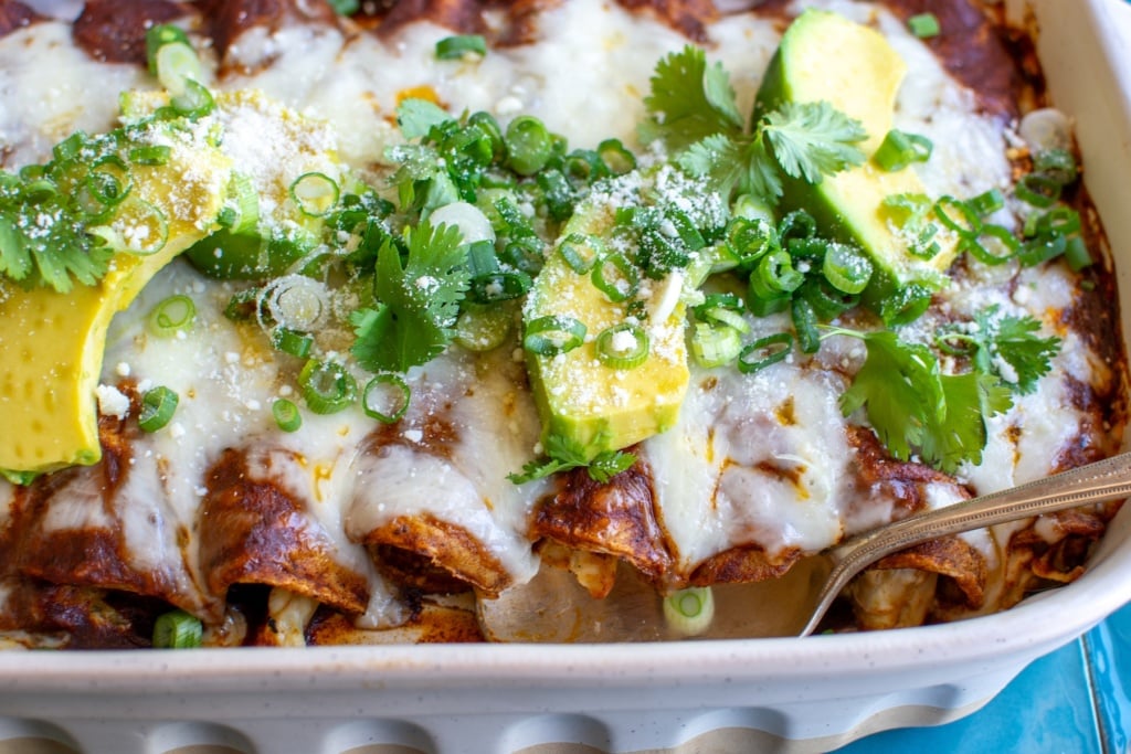 A dish of enchiladas topped with avocado and scallions 