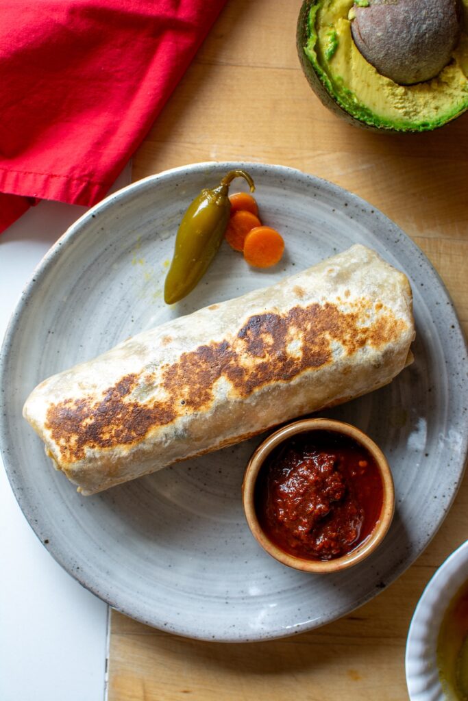 A burrito on a plate with jalapenos and carrots