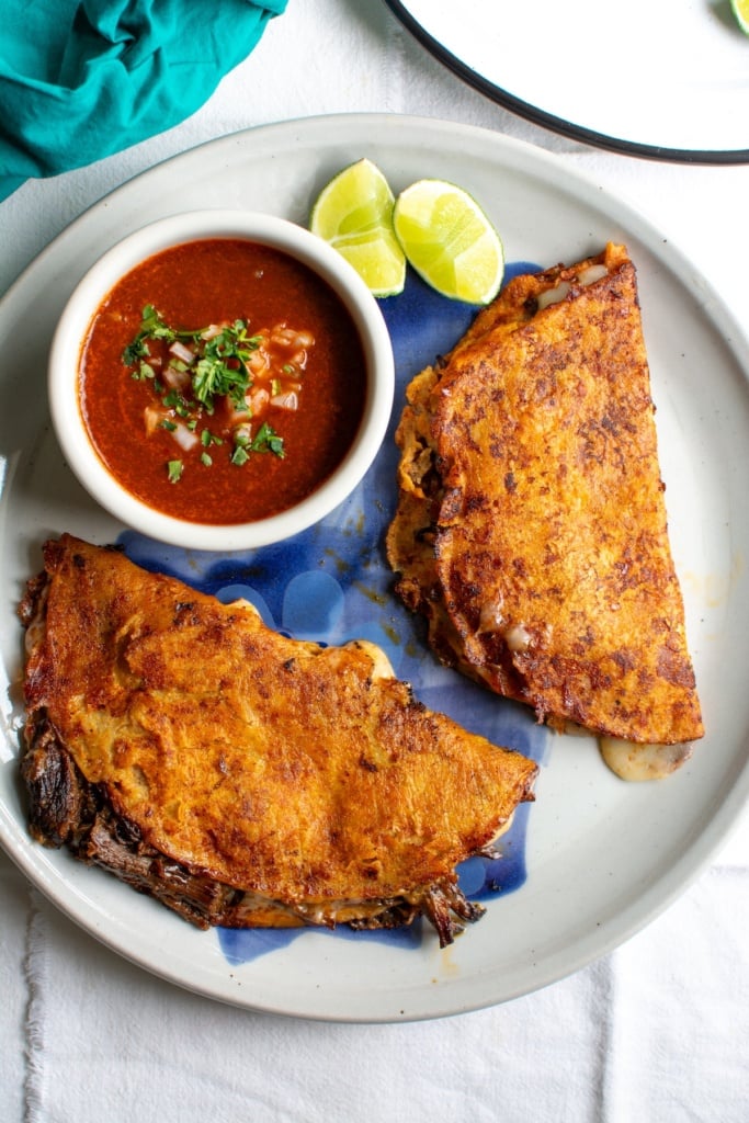 two birria tacos on a plate with consommé 