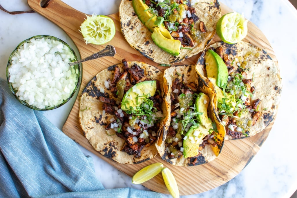 Pork adobada tacos on a cutting board next to minced onions. 