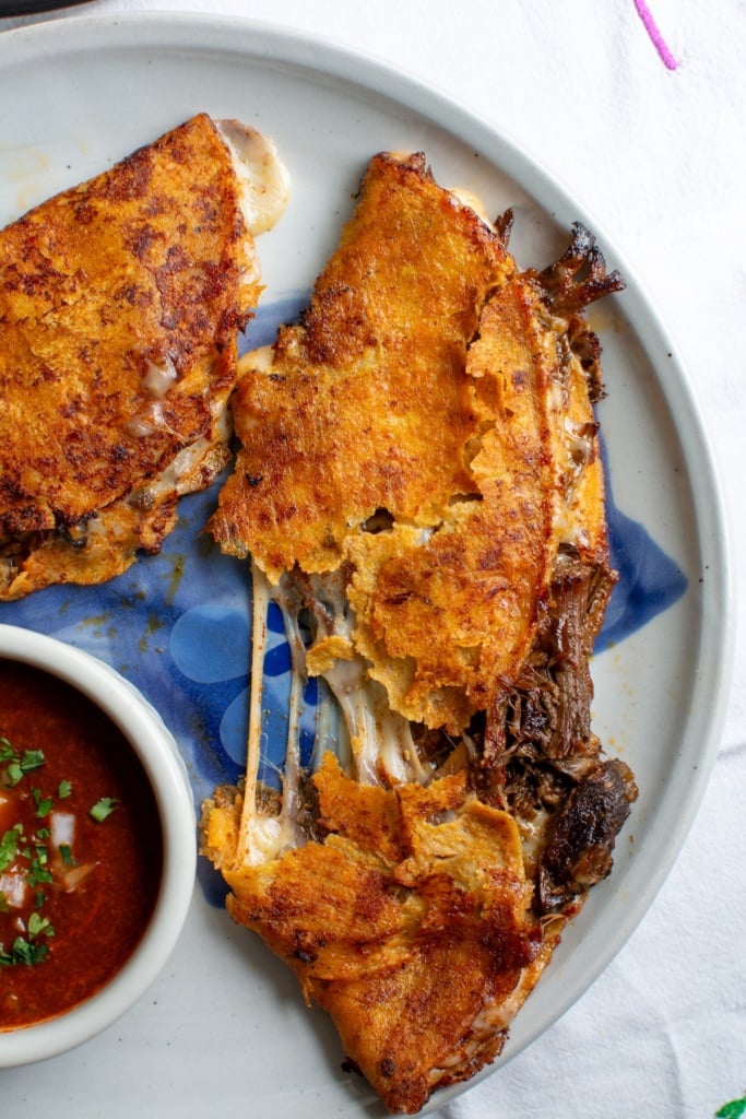 two birria tacos with one pulled apart to show the cheese