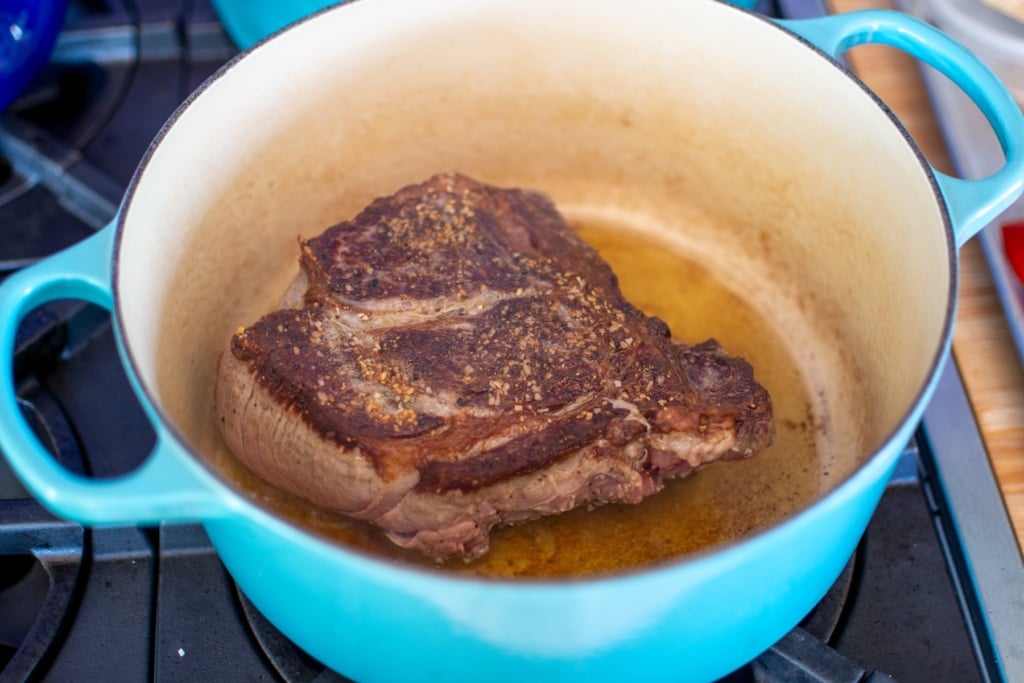 a piece of beef browning in a blue pot