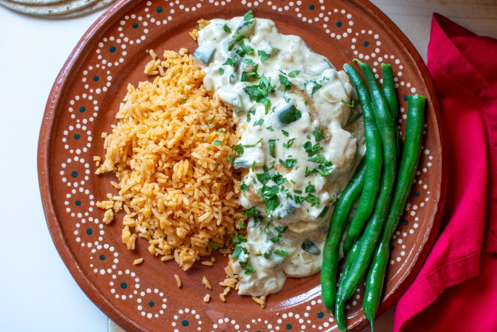 mexican pollo crema with mexican red rice and green beans on a brown plate